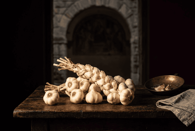 Treccia di aglio di Voghiera DOP e bulbi su legno antico, davanti all'arco affrescato di una delizia estense