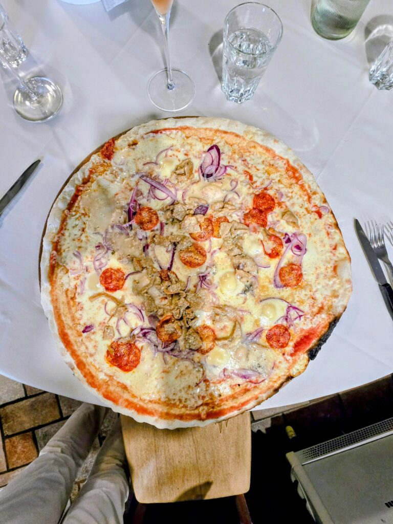 Pizza Esagerata vista dall'alto su tagliere di legno, con zola, taleggio, salame piccante, porcini e cipolla rossa, alla Trattoria da Diego di Palazzolo sull'Oglio