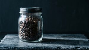 Barattolo di vetro con chicchi di caffè tostati interi su piano di ardesia nera