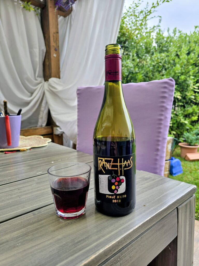 Bottiglia di Pinot Nero Alto Adige Franz Haas 2018 con calice versato su tavolo da giardino