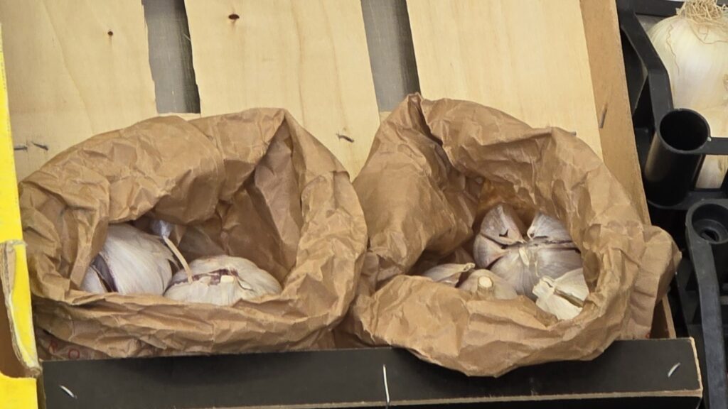 Due sacchetti di carta con bulbi d'aglio in una cassetta di legno su un banco di frutta e verdura