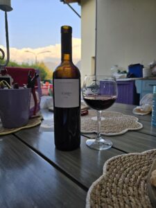 Bottiglia di Icario San Colombano DOC Rosso 2023 di Casa Valdemagna con calice servito su un tavolo all'aperto
