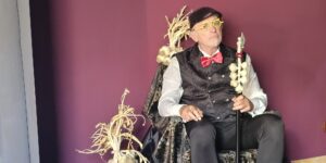 Luca Scainelli, fondatore di Vampiri Italiani, seduto su un trono nero con trecce d'aglio e un bastone sormontato da bulbi d'aglio