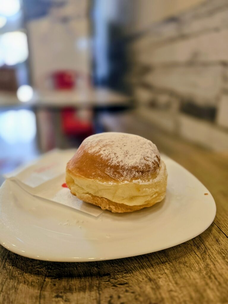 Bombolone alla crema con zucchero a velo su piatto bianco al Caffè Vespucci di Rimini