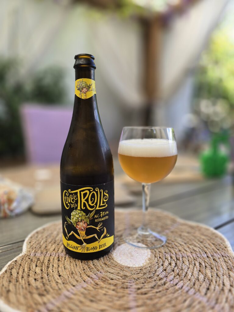 Bottiglia da 75 cl di Cuvée des Trolls di Brasserie Dubuisson accanto a un calice di birra dorata con schiuma