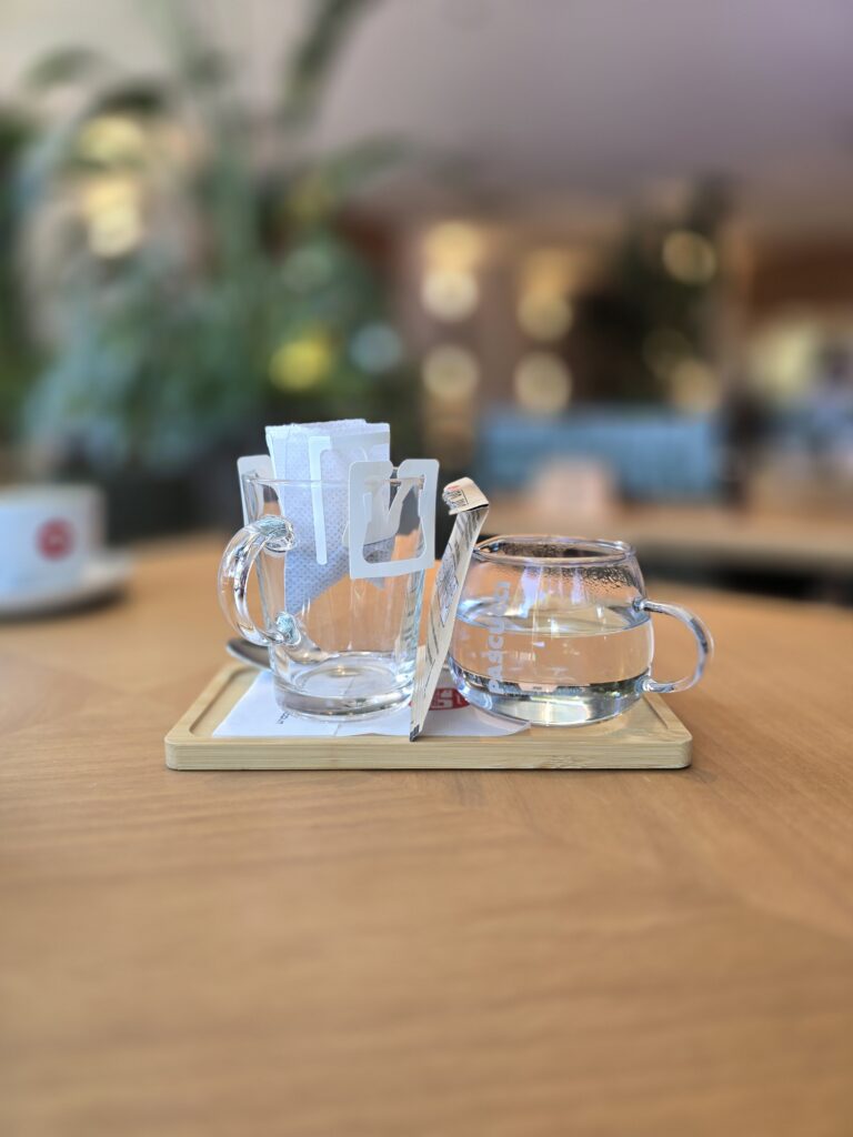 Drip coffee con filtro appeso alla tazza di vetro e brocca d'acqua su vassoio di bambù, Caffè Pascucci Rimini